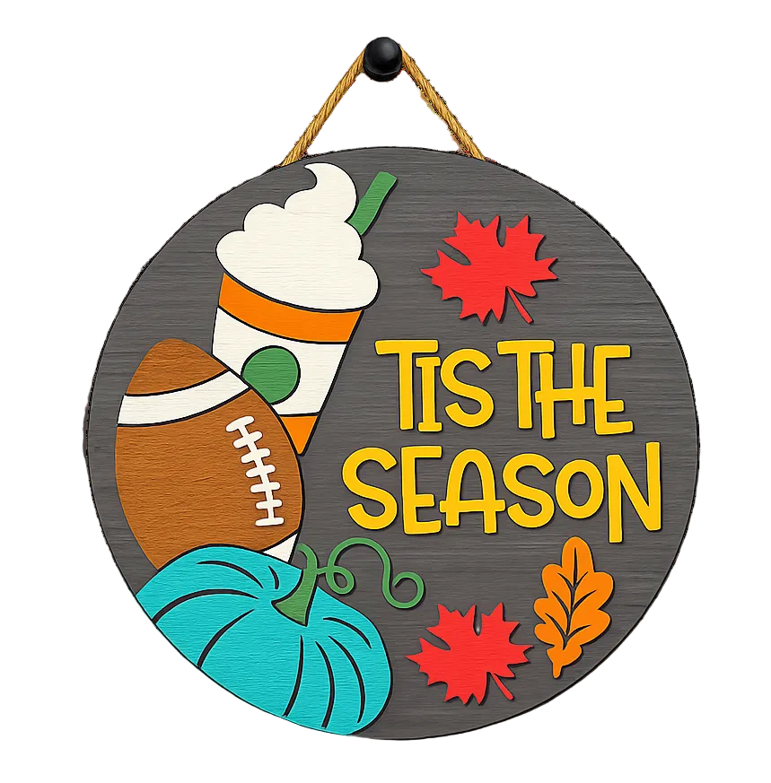 A round hanging wall sign with  the phrase “Tis the Season." The sign features autumn-themed illustrations including a pumpkin, a football, a coffee with whipped cream, red and orange leaves, and a hanging cord. Available in San Antonio TX at DIY Sign Party.